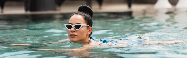 Panoramic concept of attractive young woman in sunglasses swimming in pool — Stock Photo