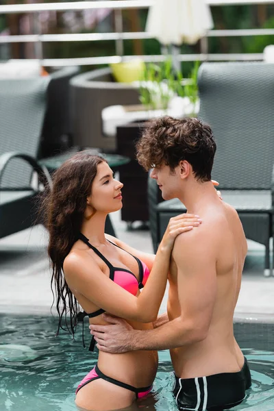 Atractiva mujer abrazando apuesto hombre sin camisa en la piscina - foto de stock