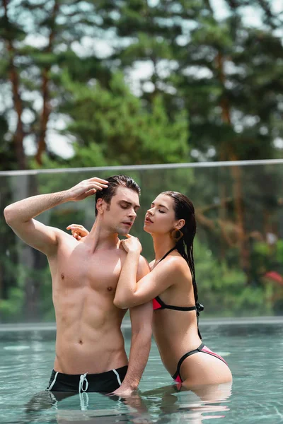 Attractive woman in swimsuit touching sexy man in swimming pool — Stock Photo