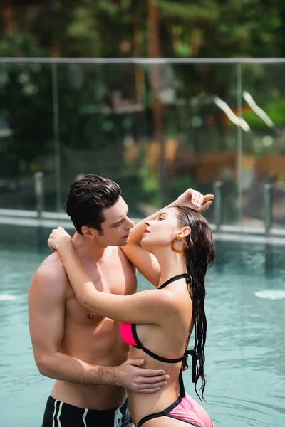 Homem sem camisa olhando para menina sensual em maiô de pé na piscina — Fotografia de Stock