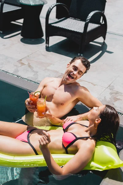 Woman lying on inflatable mattress and clinking cocktails with cheerful man — Stock Photo