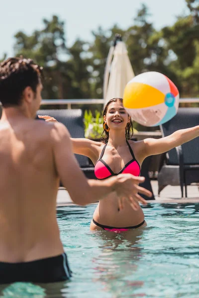 Messa a fuoco selettiva di ragazza e uomo a torso nudo giocare a pallavolo con pallone da spiaggia in piscina — Foto stock