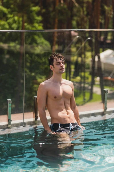 Handsome and shirtless man in swim trunks standing in swimming pool — Stock Photo