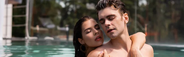 Tiro panorámico de mujer joven abrazando hombre musculoso en la piscina - foto de stock