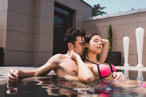 Hombre guapo oliendo pelo de mujer atractiva en la piscina - foto de stock