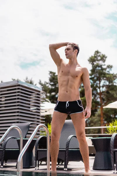 Homme torse nu touchant les cheveux et debout près de la piscine — Photo de stock
