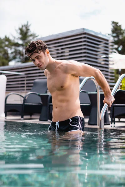 Selective focus of shirtless man standing on pool ladder in swimming pool — Stock Photo