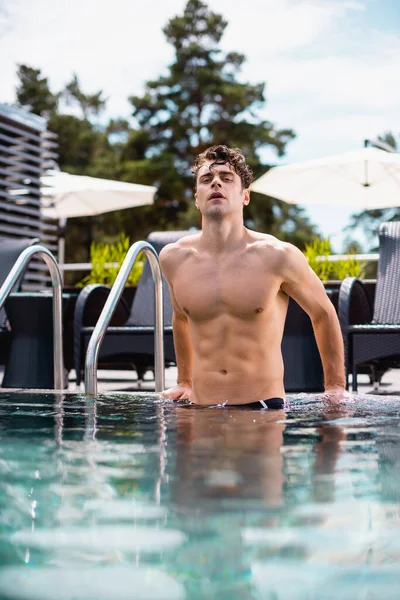 Messa a fuoco selettiva di uomo sexy e muscoloso guardando la fotocamera in piscina — Foto stock