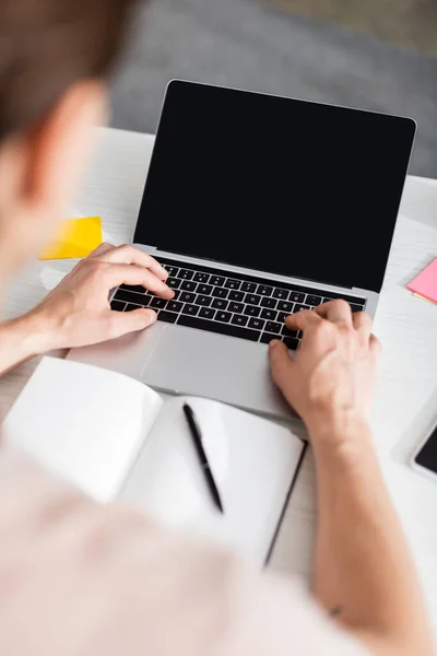 Vista recortada del hombre escribiendo en el ordenador portátil con pantalla en blanco, sentado en la mesa en casa, ganando concepto en línea - foto de stock