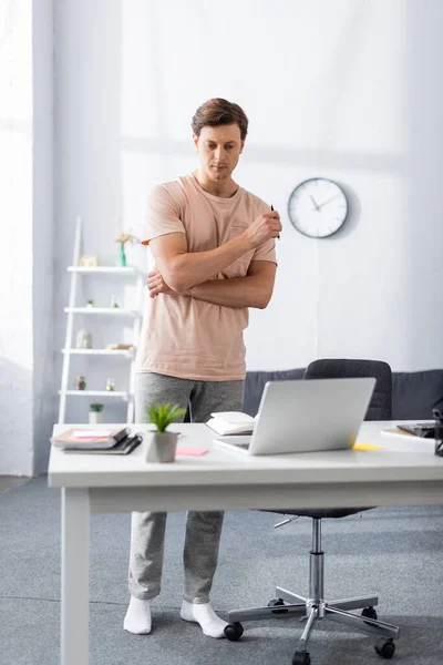 Front view of thinking freelancer near laptop and stationery on table at home, earning online concept — Stock Photo