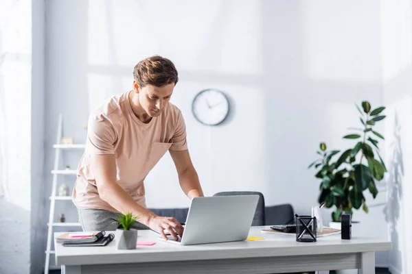 Handsome freelancer leaning forward and typing on laptop at home, earning online concept — Stock Photo