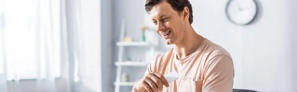 Panoramic shot of smiling freelancer holding smartphone at home — Stock Photo