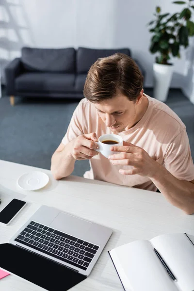 Visão aérea do homem bebendo café e olhando para a tela do laptop em casa, ganhando conceito online — Fotografia de Stock