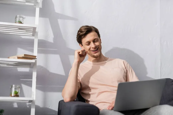 Selective focus of smiling freelancer using laptop on couch at home, concept of earning online — Stock Photo