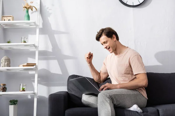 Positive man showing yeah gesture while using laptop in living room, concept of earning online — Stock Photo