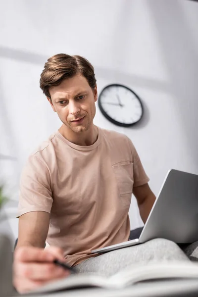 Selective focus of teleworker writing on notebook and holding laptop at home, concept of earning online — Stock Photo