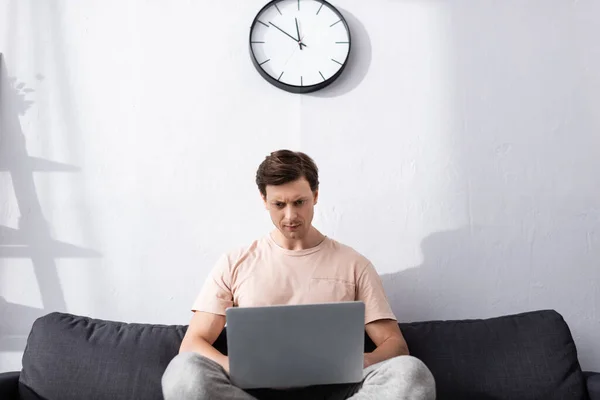 Focus selettivo di freelance concentrato utilizzando il computer portatile mentre seduto sul divano a casa, concetto di guadagnare online — Foto stock