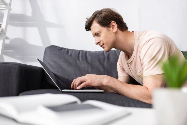 Focus selettivo del bel freelance che utilizza laptop sul divano a casa, guadagnando concetto online — Foto stock