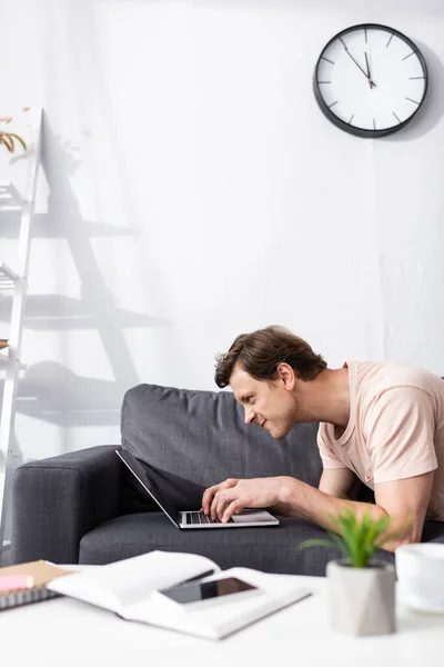 Enfoque selectivo de freelancer enojado utilizando un ordenador portátil cerca de teléfonos inteligentes y portátiles en la mesa de café en casa, ganando concepto en línea — Stock Photo