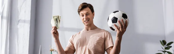 Панорамний урожай позитивного чоловіка, який тримає гроші і футбол вдома — стокове фото