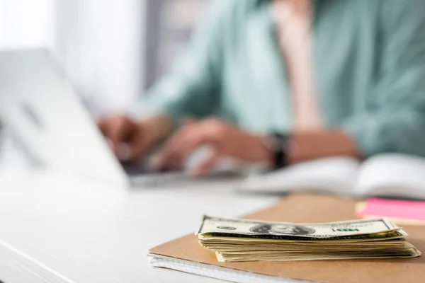 Selective focus of dollars on notebook and man using laptop at table, concept of earning online — Stock Photo