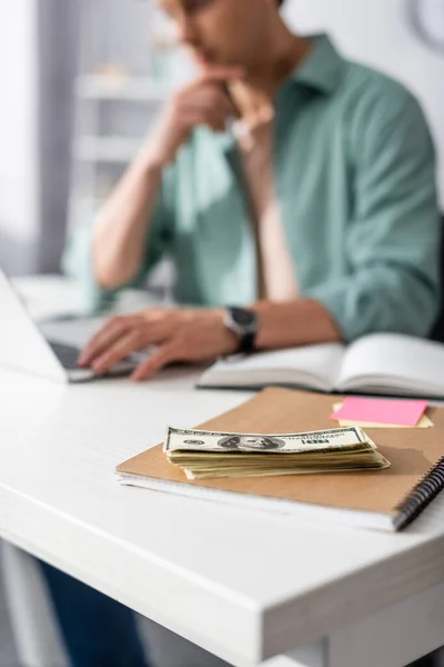 Enfoque selectivo de dinero en efectivo en notebook y freelancer utilizando el ordenador portátil en la mesa, concepto de ganar en línea - foto de stock