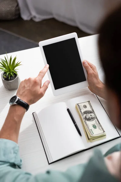 Selektiver Fokus des jungen Mannes mit digitalem Tablet in der Nähe von Bargeld auf offenem Notizbuch auf dem Tisch, verdienen Online-Konzept — Stockfoto