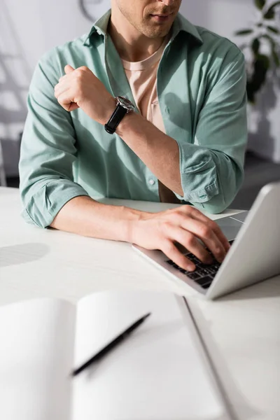 Vista recortada del hombre usando portátil cerca de portátil abierto con pluma en la mesa - foto de stock