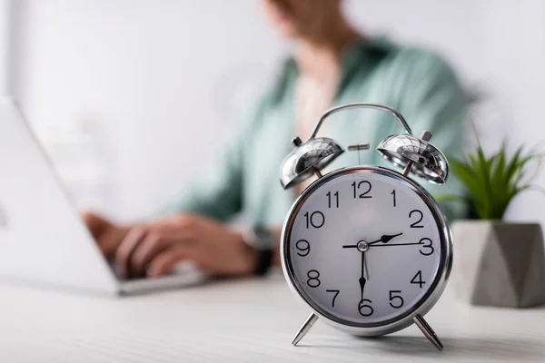 Selective focus of alarm clock on table near man using laptop at home, concept of time management — Stock Photo