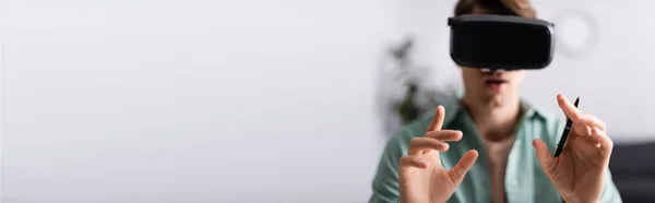 Panoramic crop of man in virtual reality headset holding pen at home — Stock Photo