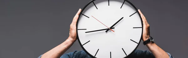 Panoramic crop of man holding clock near face isolated on grey, concept of time management — Stock Photo