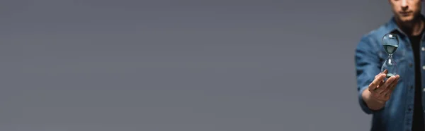 Panoramic crop of young man holding hourglass isolated on grey, concept of time management — Stock Photo