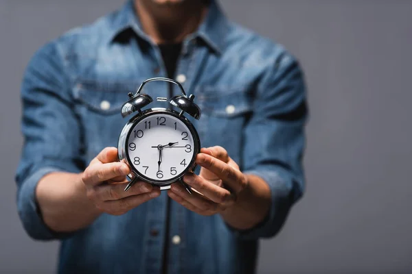 Vista recortada del hombre mostrando el reloj despertador aislado en gris, concepto de gestión del tiempo - foto de stock