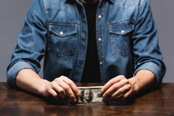 Cropped view of young man holding dollars at table isolated on grey — Stock Photo