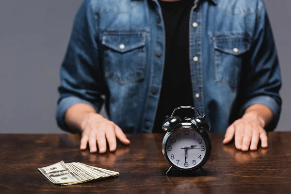 Foco seletivo de dólares e despertador na mesa perto do homem isolado no cinza, conceito de gerenciamento de tempo — Fotografia de Stock