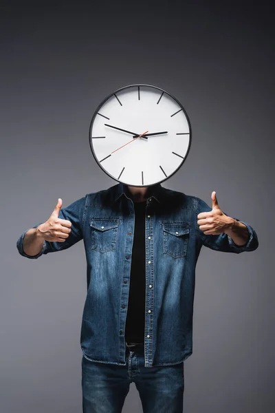 Hombre con el reloj cerca de la cara mostrando pulgares hacia arriba sobre fondo gris, concepto de gestión del tiempo - foto de stock