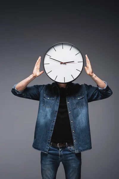 Jeune homme en jean veste avec horloge sur la tête sur fond gris, concept de gestion du temps — Photo de stock
