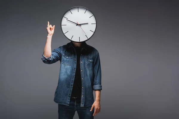 Man with clock near face pointing with fingers on grey background, concept of time management — Stock Photo