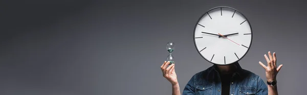 Vue panoramique de l'homme avec horloge sur la tête tenant sablier et geste sur fond gris, concept de gestion du temps — Photo de stock