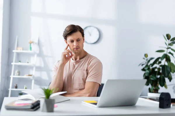 Enfoque selectivo del hombre reflexivo mirando el ordenador portátil mientras trabaja en casa, ganando concepto en línea - foto de stock