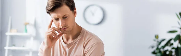 Orientación panorámica del hombre pensativo con la mano cerca de la mejilla mirando hacia otro lado en casa - foto de stock