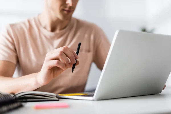 Cropped view of freelancer holding pen and using laptop on table, earning online concept — Stock Photo