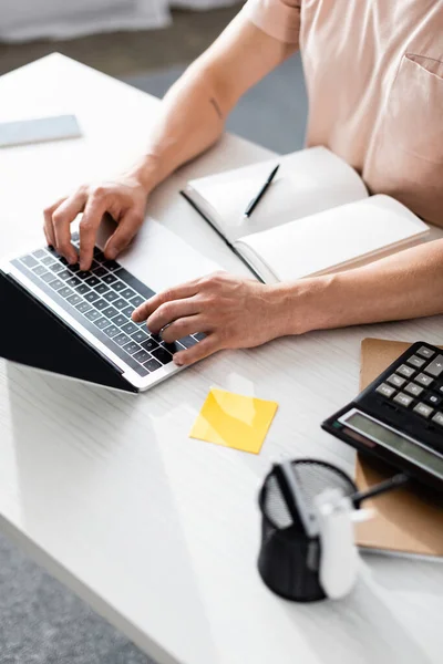 Vista recortada del freelancer usando el ordenador portátil con la pantalla en blanco cerca de la calculadora y los cuadernos en la mesa, ganando concepto en línea - foto de stock