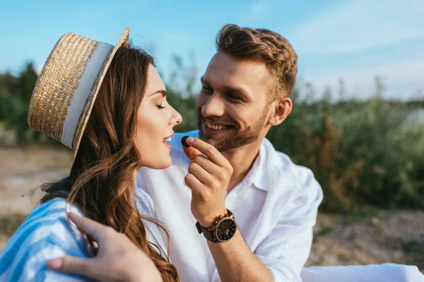 Щасливий чоловік тримає виноград біля красивої дівчини з закритими очима — стокове фото