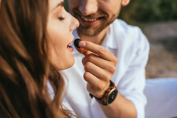 Enfoque selectivo de hombre feliz sosteniendo uva cerca de hermosa chica con los ojos cerrados - foto de stock