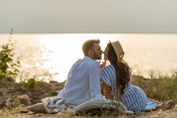 Vue latérale de bel homme et belle femme en chapeau de paille assis près du lac — Photo de stock