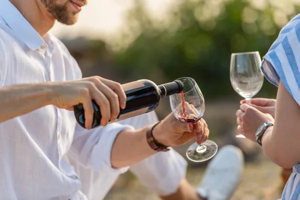 Обрізаний вид бородатого чоловіка, який тримає пляшку, поливаючи червоне вино в склянці біля жінки — стокове фото