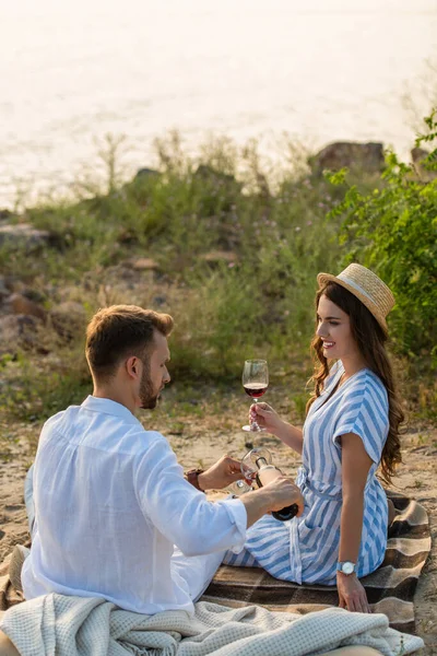 Uomo barbuto in possesso di bottiglia, mentre versando vino rosso in vetro vicino donna felice — Foto stock