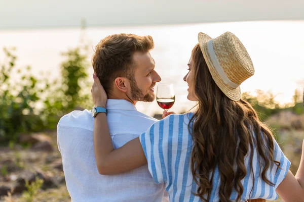 Donna allegra in cappello di paglia toccare fidanzato felice in possesso di vetro con vino rosso — Foto stock