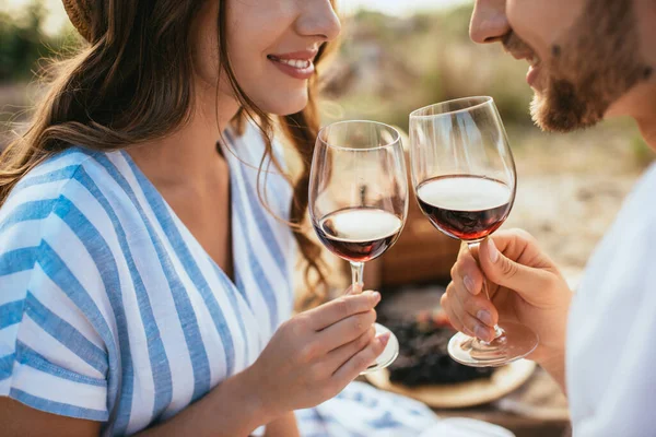 Vue recadrée du couple gai cliquetis verres avec vin rouge — Photo de stock